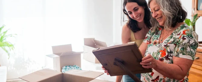 Senior mother smiles while unpacking family photos in their new assisted living apartment at The Sequoia Senior Living in Olympia, WA.