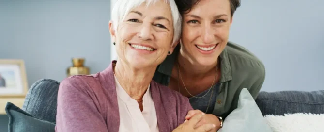 Time for assisted living: adult daughter smiles with senior mother at home on couch