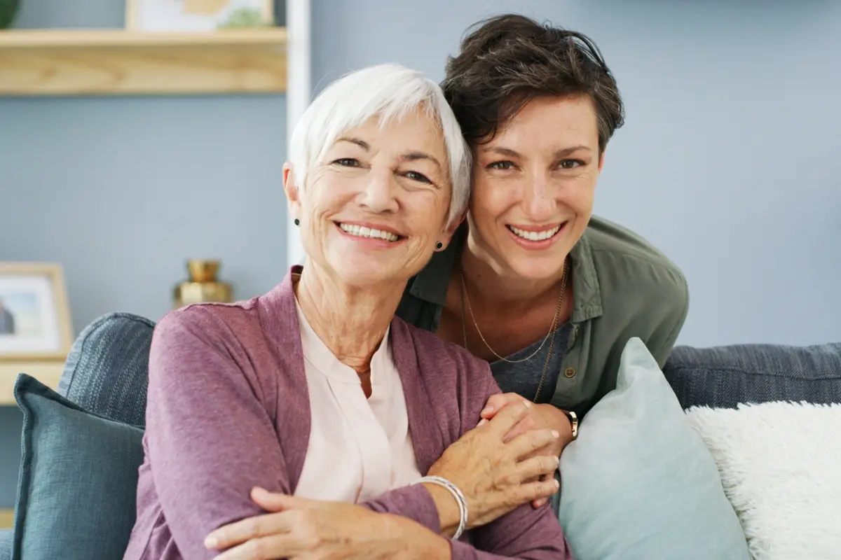 Time for assisted living: adult daughter smiles with senior mother at home on couch