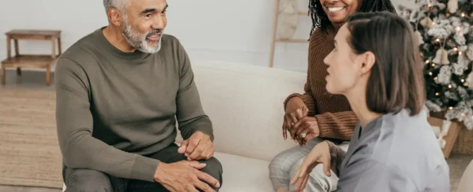Assisted living memory care vs nursing home: caregiver talks with senior couple on couch
