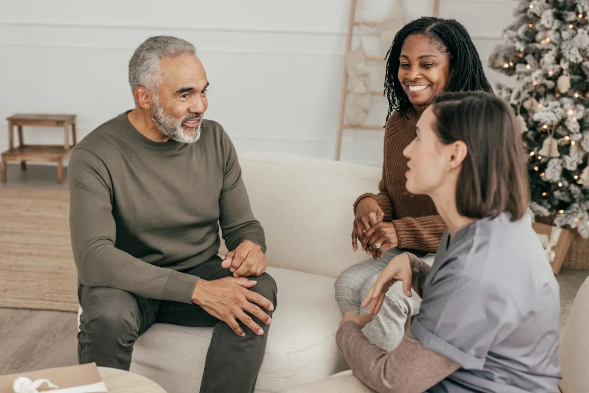 Assisted living memory care vs nursing home: caregiver talks with senior couple on couch